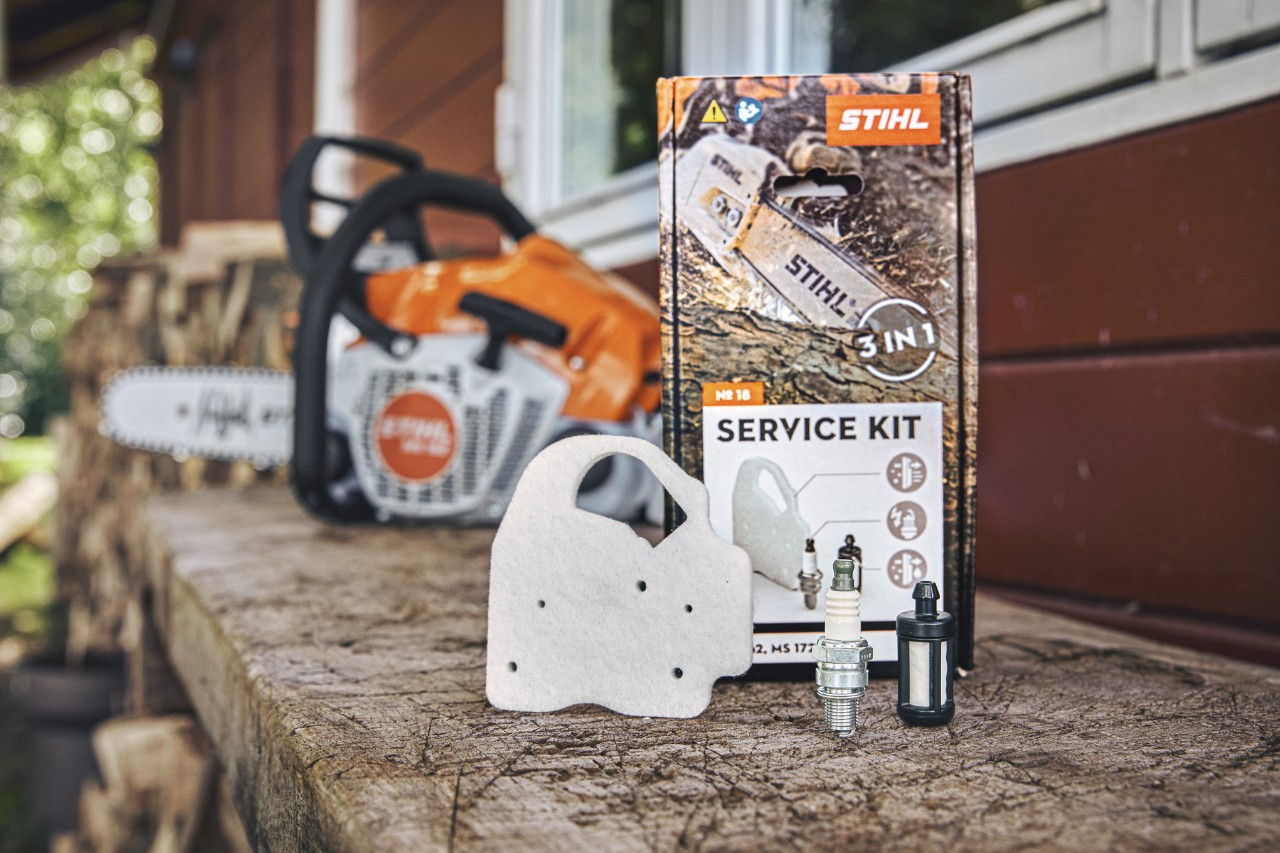 STIHL Service Kit 18 on a workbench, in front of it the individual components fleece air filter, spark plug and fuel filter