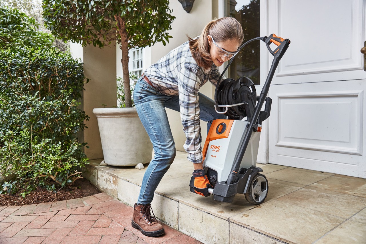 Kobieta znosi myjkę wysokociśnieniową STIHL RE 130 plus na schodach przed drzwiami mieszkania