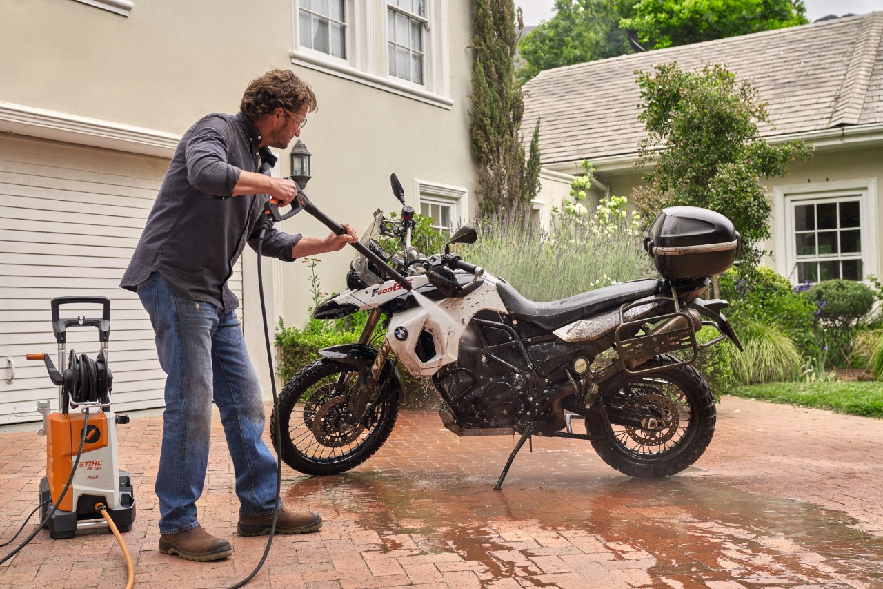 Mężczyzna na podjeździe do garażu czyści motocykl myjką wysokociśnieniową STIHL  