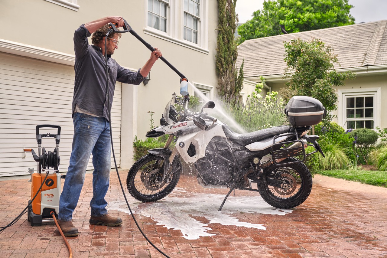 Mężczyzna spryskuje motocykl środkiem do czyszczenia pojazdów za pomocą myjki wysokociśnieniowej STIHL RE 130 plus, aby go wyczyścić