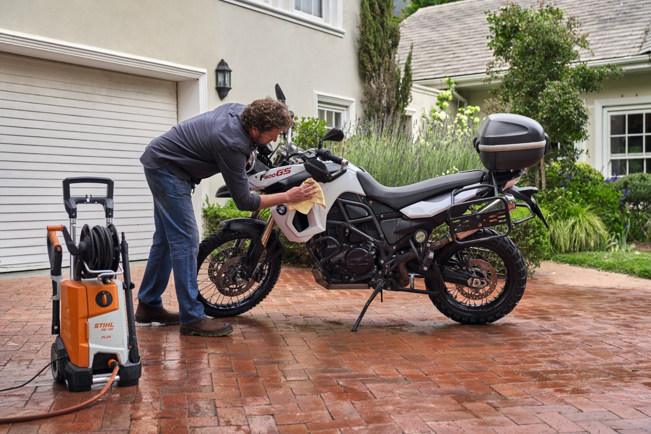 Mężczyzna osusza motocykl po czyszczeniu, obok niego stoi myjka wysokociśnieniowa STIHL RE 130 plus