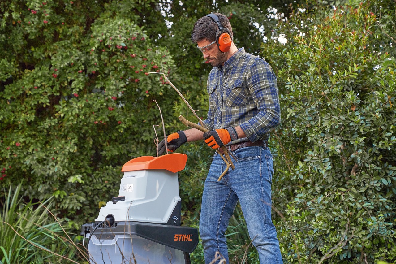 Mężczyzna w odzieży ochronnej rozdrabnia gałęzie rozdrabniaczem ogrodowym STIHL  