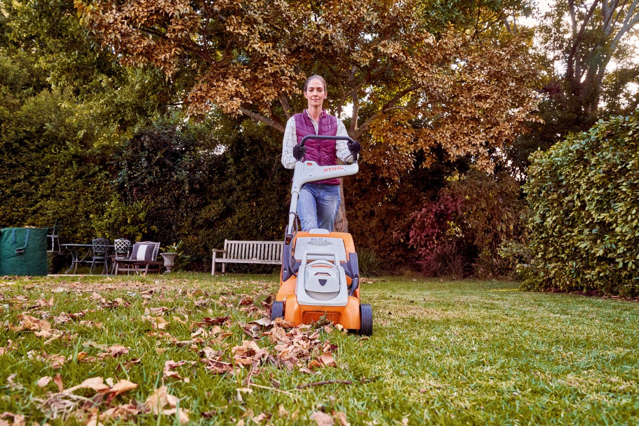 Frau mäht den laubbedeckten Rasen im Garten im Herbst mit dem STIHL Akku-Rasenmäher RMA 339 C.
