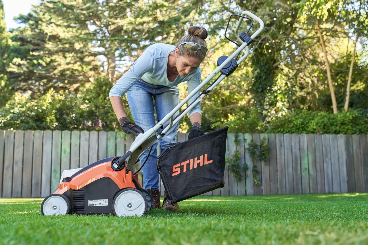Kobieta zawiesza kosz zbierający akumulatorowego aeratora do trawnika STIHL RLA 240 z tyłu urządzenia.