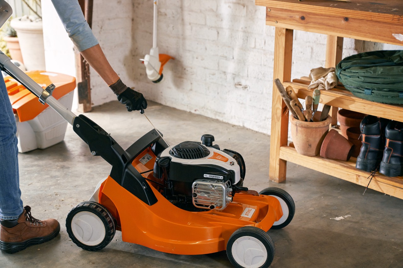 Osoba czyszcząca filtr powietrza kosiarki benzynowej STIHL RM 448 TC w garażu