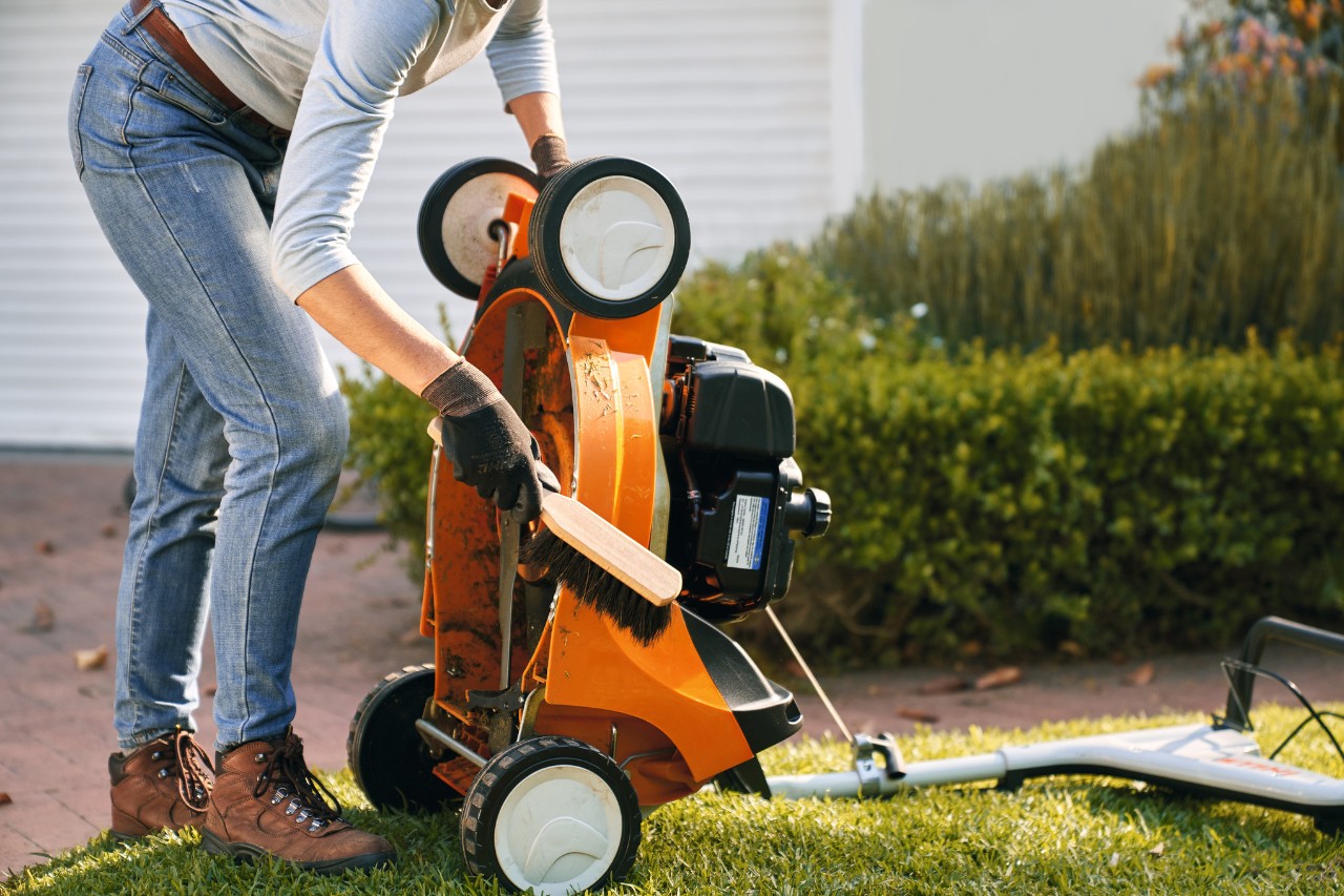 Kobieta czyści kosiarkę benzynową STIHL RM 448 TC zmiotką