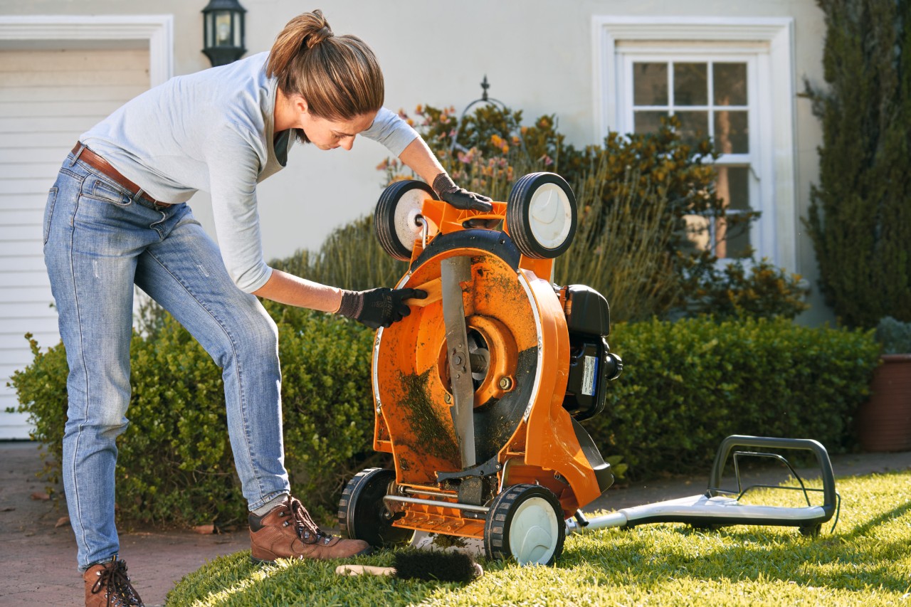Kobieta czyści podwozie benzynowej kosiarki do trawy STIHL RM 448 T-C za pomocą szpatułki