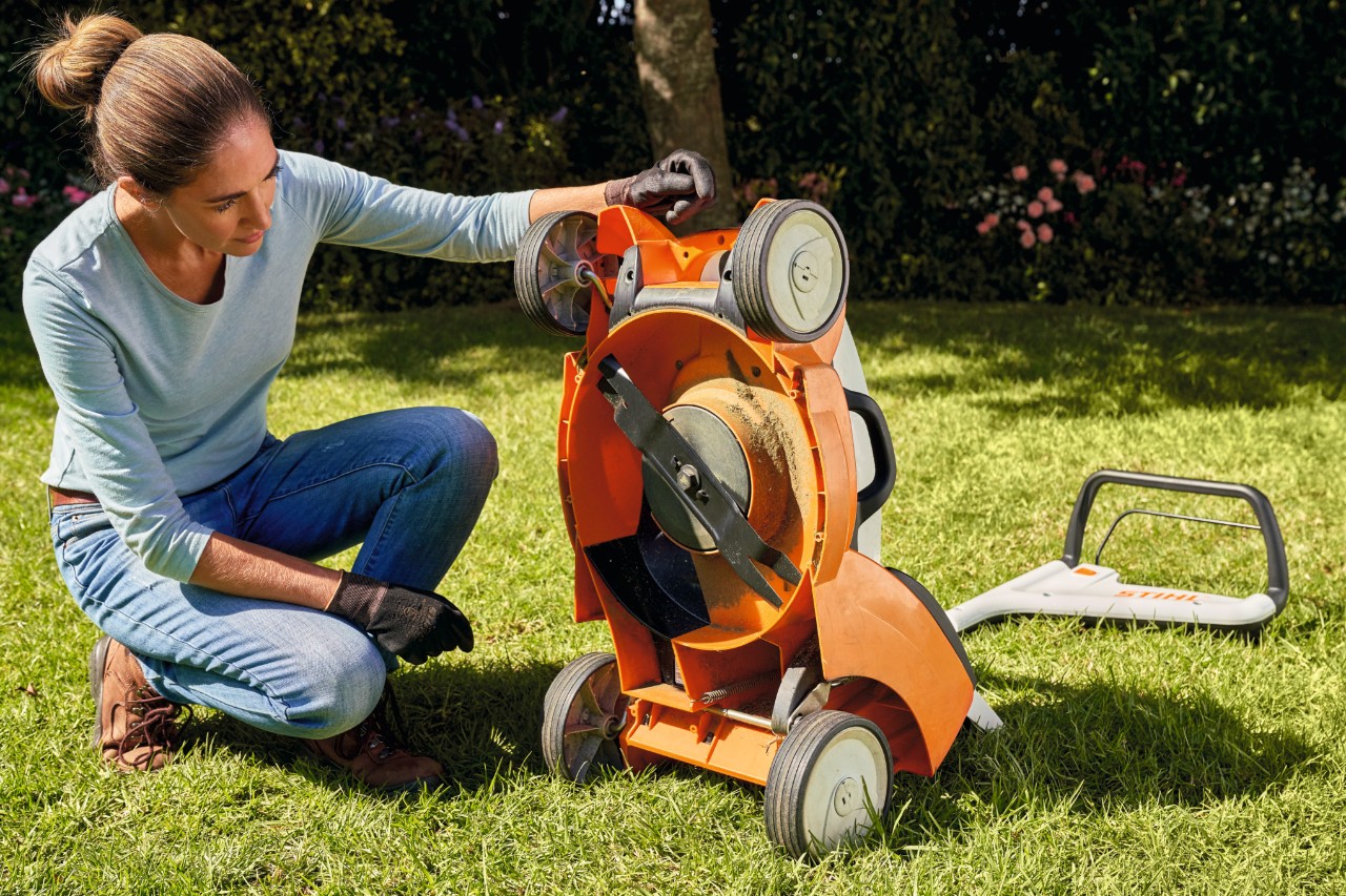 Klęcząca kobieta patrzy na zespół koszący kosiarki STIHL RMA 399 C.