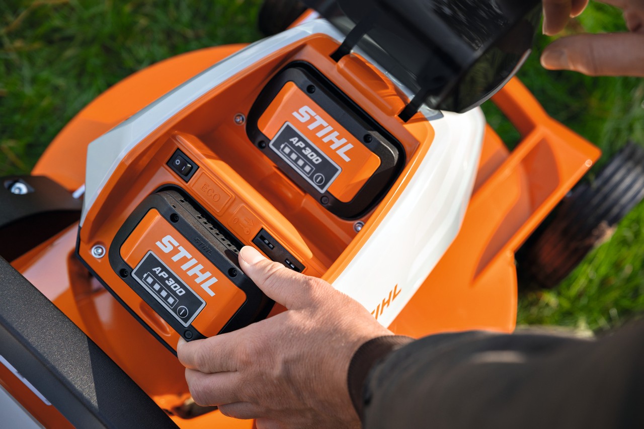 Osoba wkłada w pełni naładowany akumulator STIHL AP 300 do kosiarki