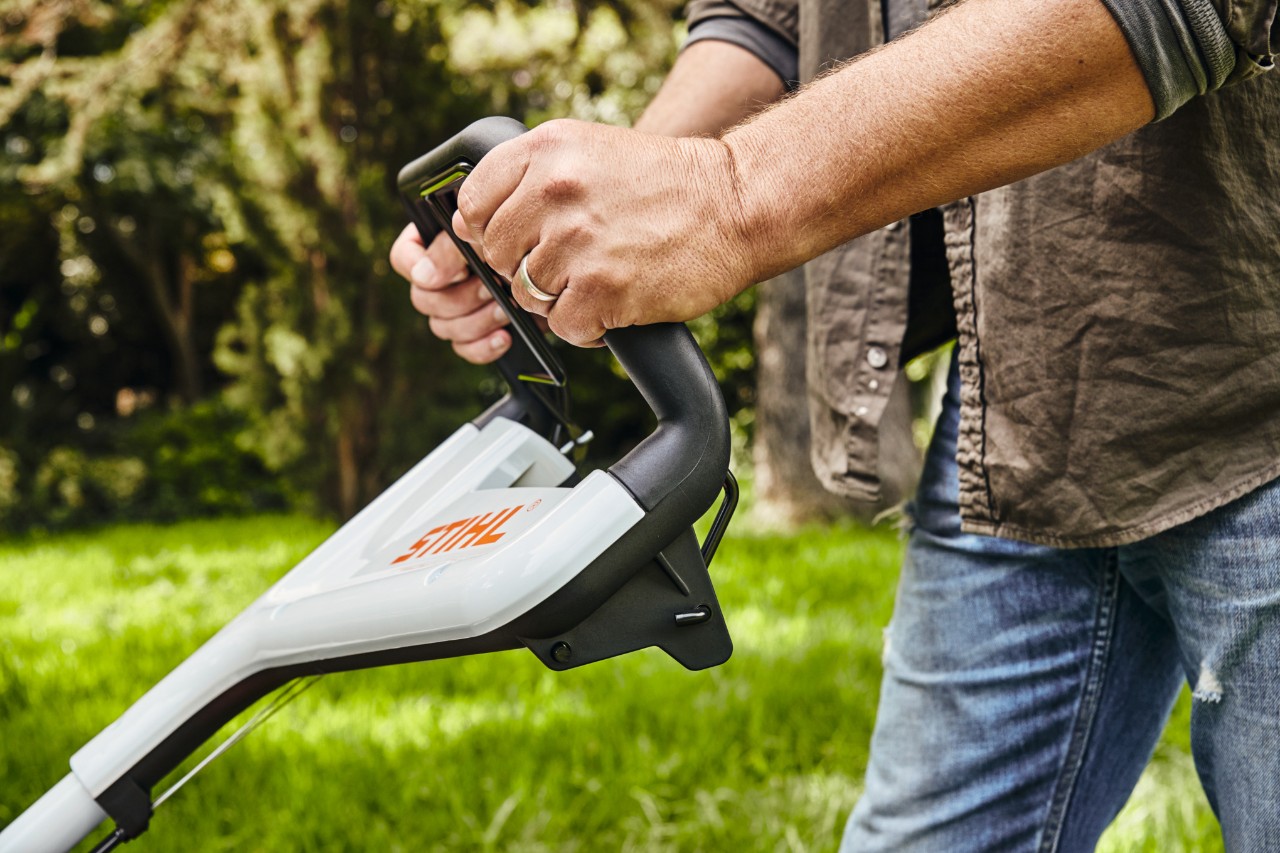 Mężczyzna trzyma kosiarkę benzynową STIHL RM 448 TC za kierownicę, aby skosić trawnik