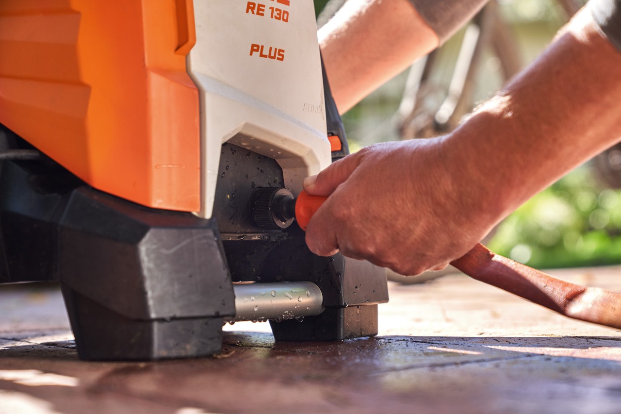 Osoba podłączająca wąż ogrodowy do myjki wysokociśnieniowej STIHL RE 130 PLUS w celu jej użycia