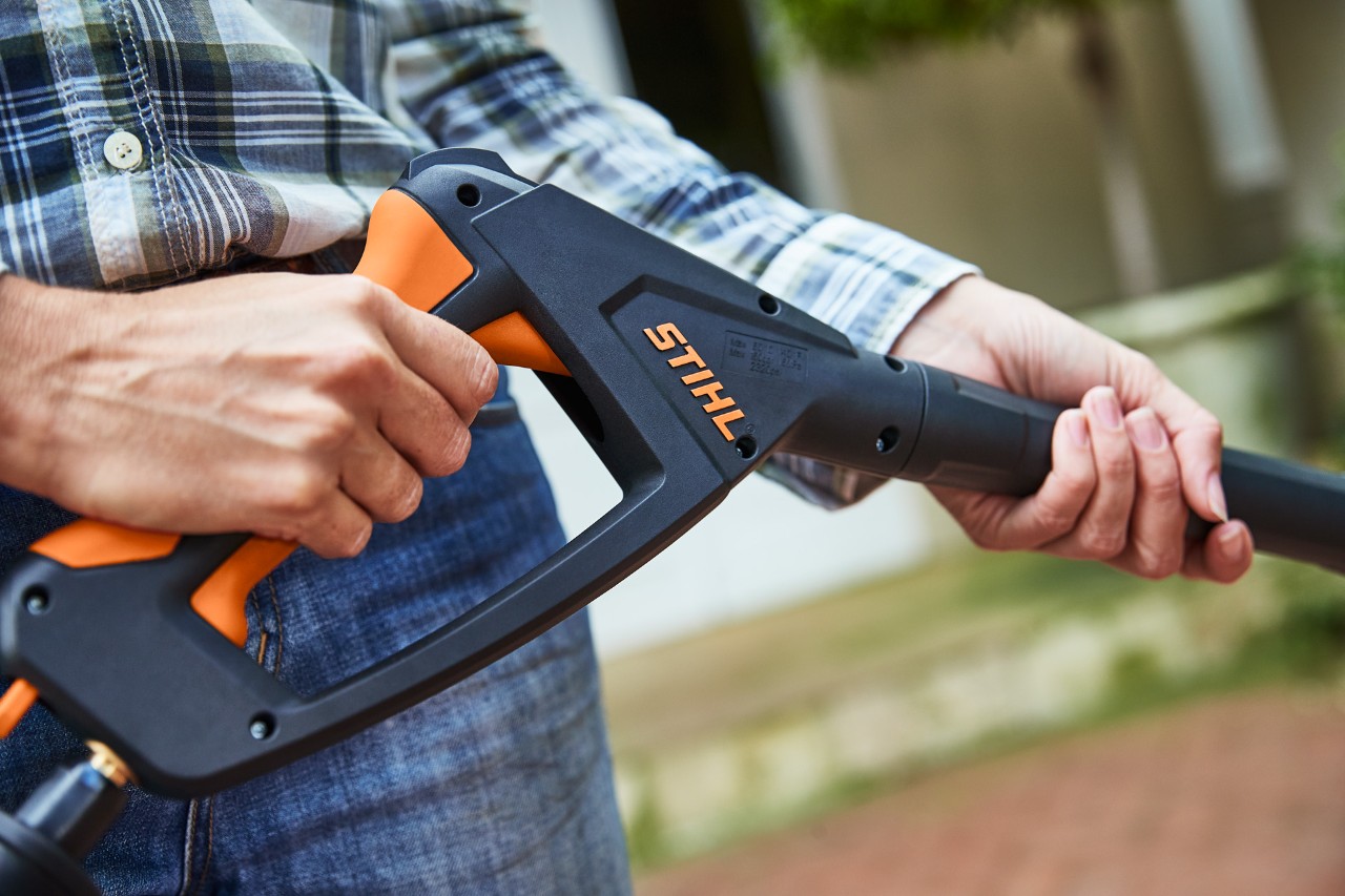 Osoba obsługuje myjkę wysokociśnieniową STIHL RE 130 PLUS, trzymając spust pistoletu natryskowego