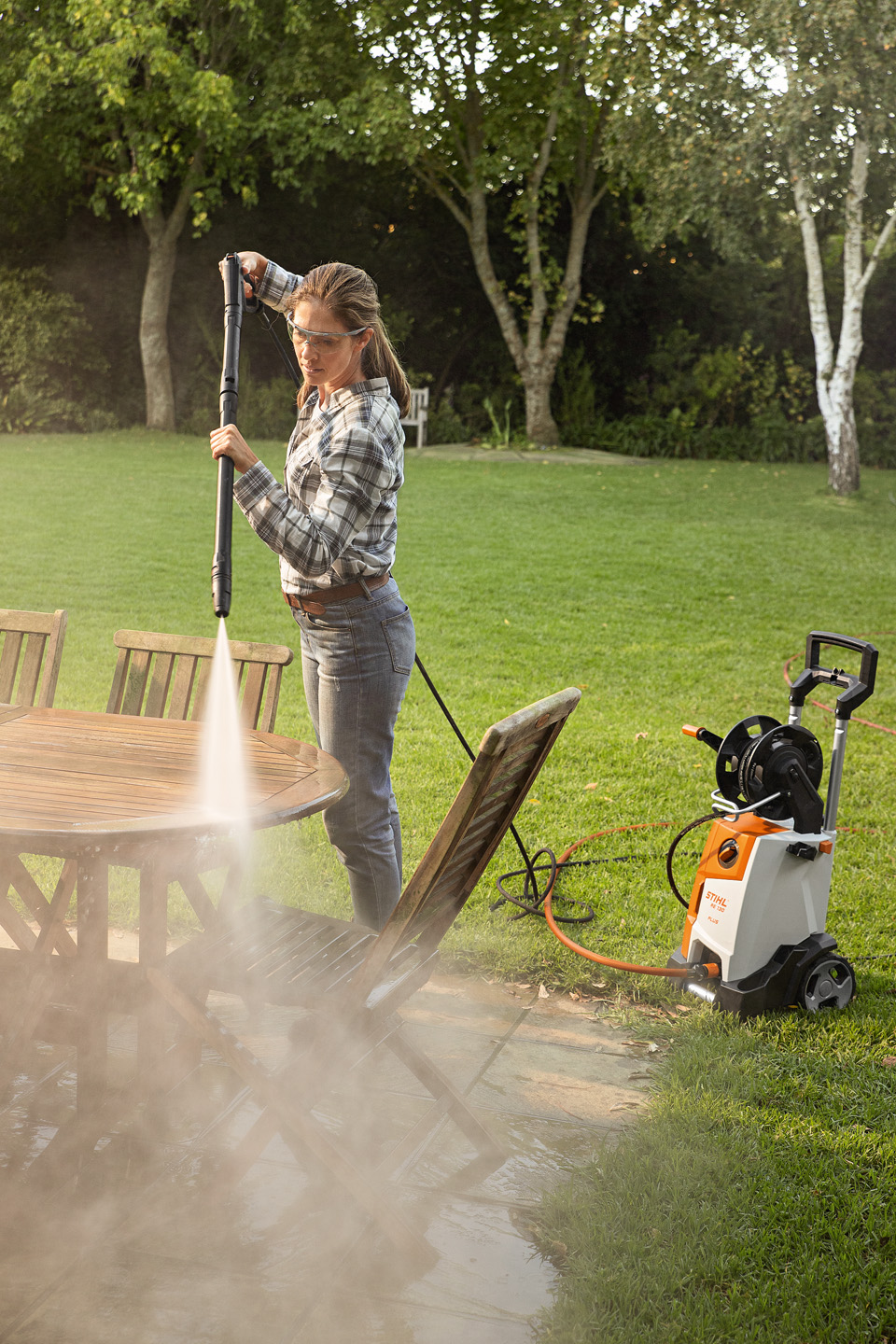 Kobieta używająca myjki wysokociśnieniowej STIHL RE 130 PLUS na zewnątrz do czyszczenia mebli ogrodowych