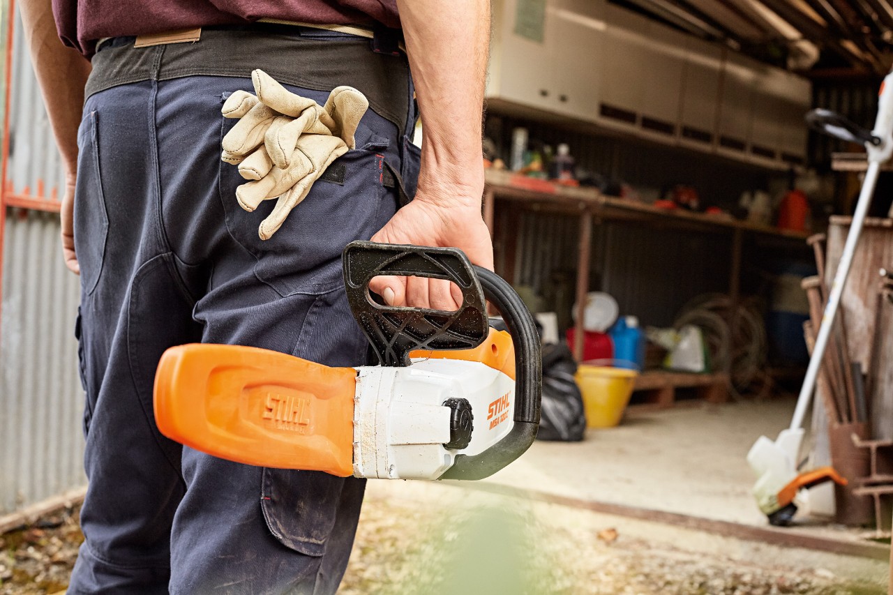 Mężczyzna stoi przed warsztatem z akumulatorową pilarką łańcuchową STIHL z osłoną prowadnicy