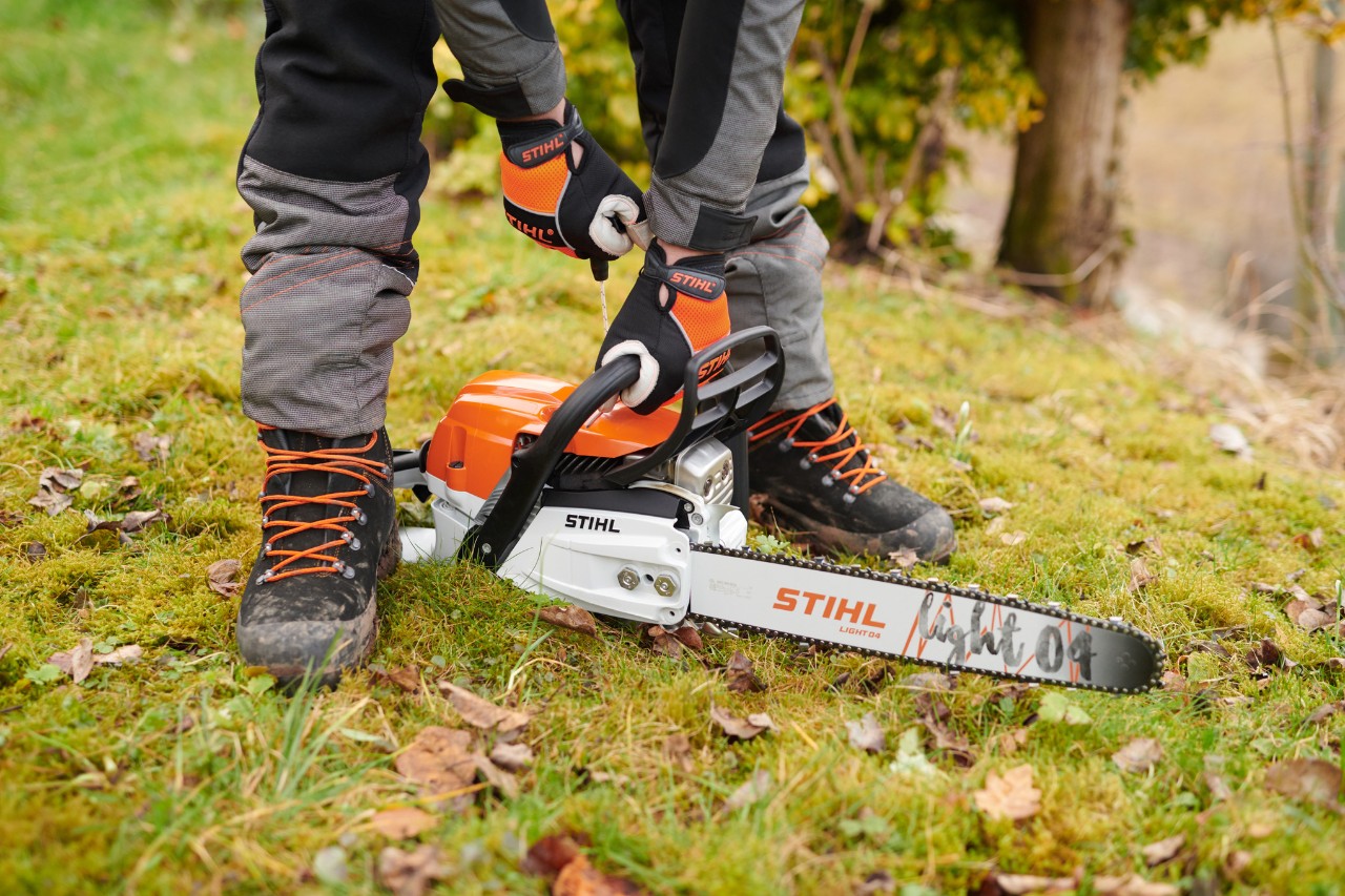 Pilarka STIHL MS261CM stoi stabilnie na podłożu w lesie i może zostać bezpiecznie uruchomiona.
