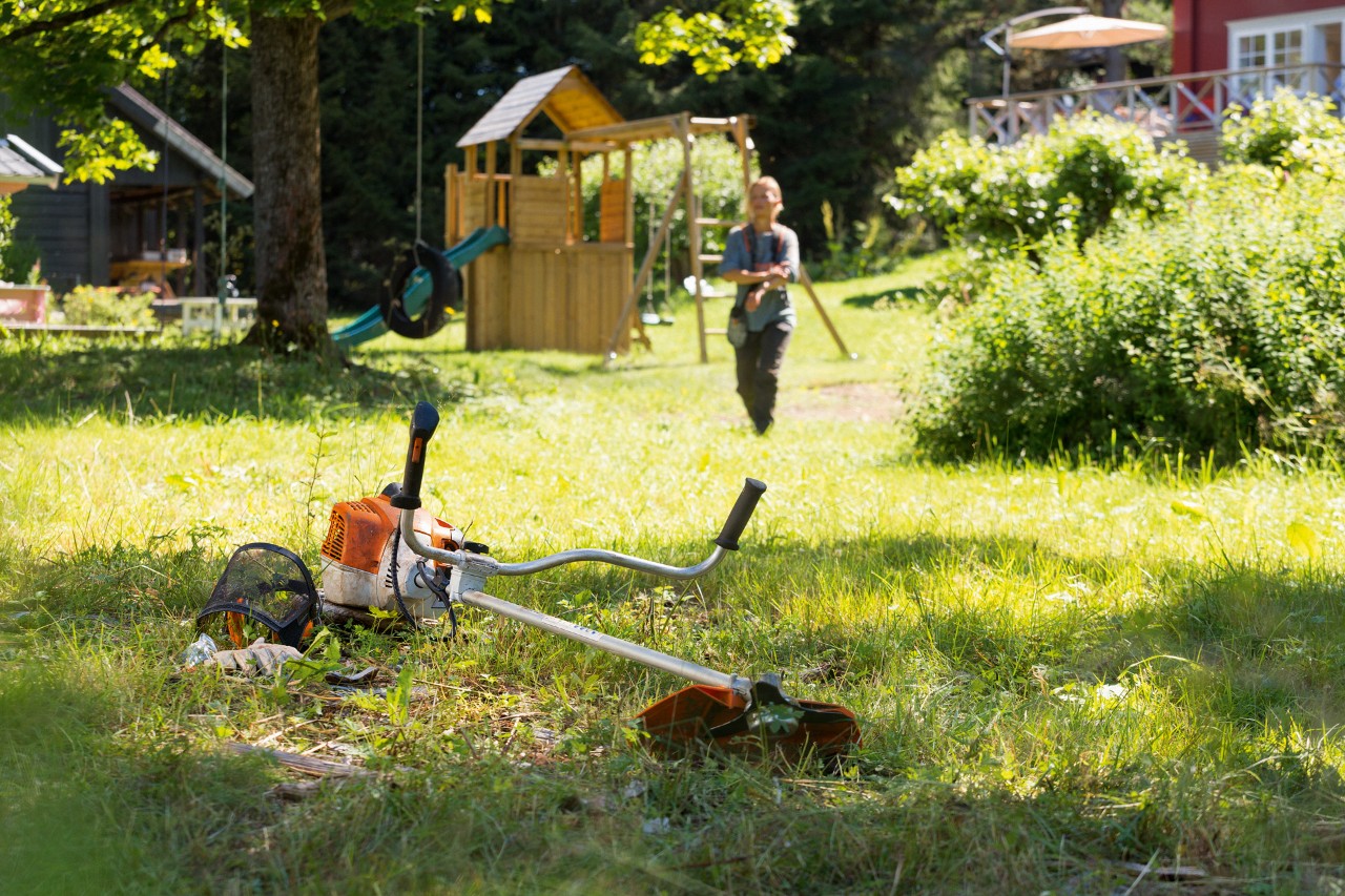Kosa mechaniczna STIHL FS 240 w trawie, w tle mężczyzna przygotowuje się do konserwacji