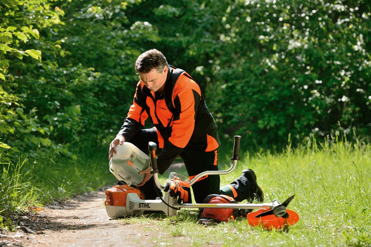 Mężczyzna w sprzęcie ochronnym STIHL tankuje kosę mechaniczną mieszanką benzyny i oleju