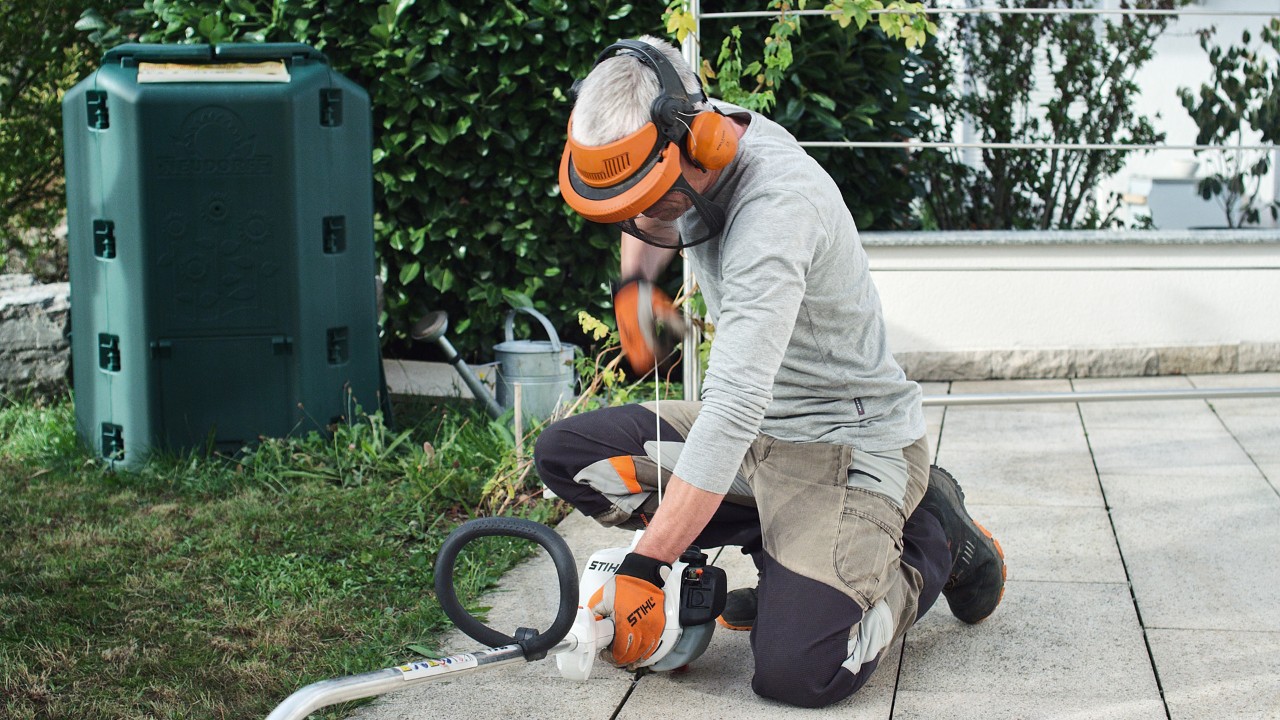 Osoba w odzieży ochronnej ciągnie linkę rozrusznika benzynowej kosy mechanicznej STIHL FS 38