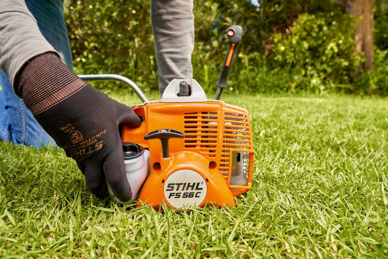 Mężczyzna naciskający pompę paliwa benzynowej kosy mechanicznej STIHL FS 56, aby ją uruchomić