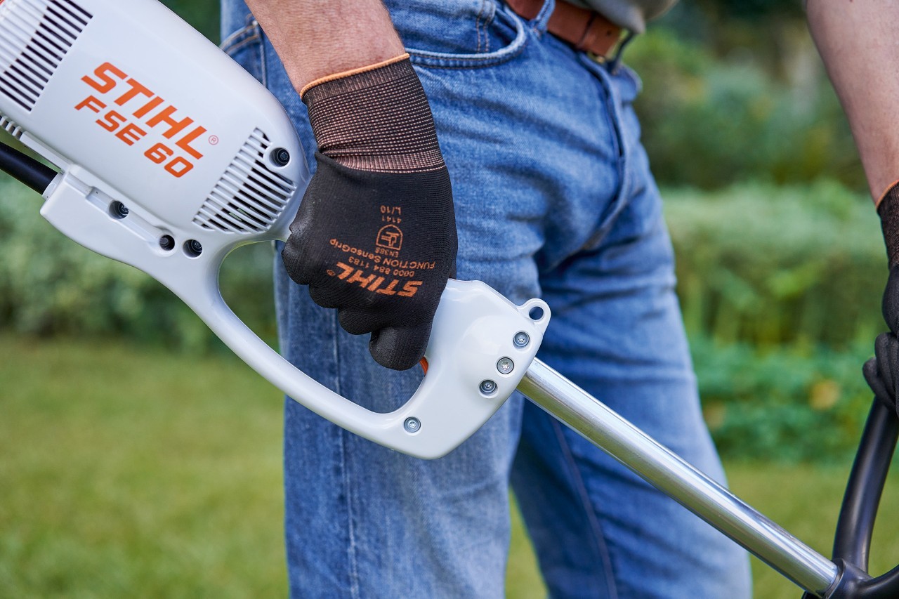 Mężczyzna naciska przycisk na uchwycie obsługowym elektrycznej kosy mechanicznej STIHL FSE 60