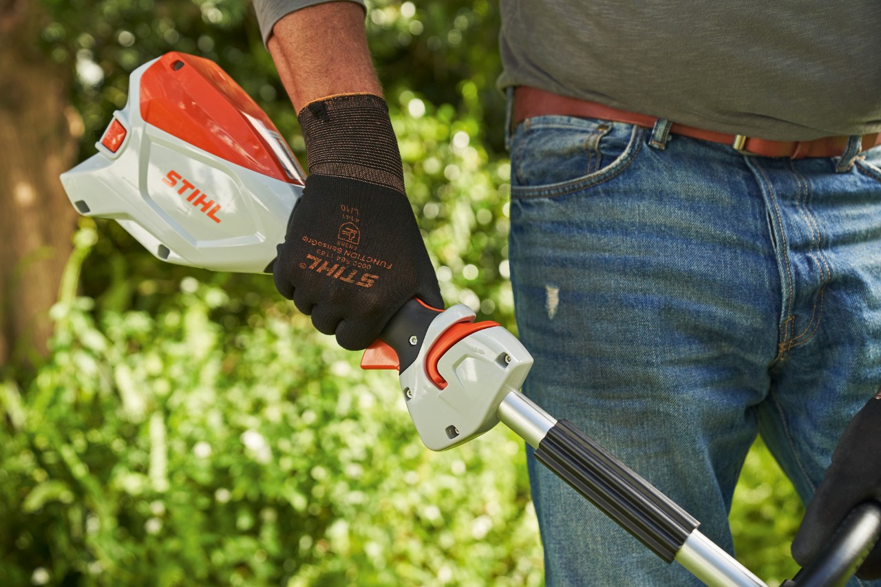 Mężczyzna w rękawicach ochronnych naciska blokadę dźwigni zmiany prędkości w akumulatorowej kosie mechanicznej STIHL FSA 60 