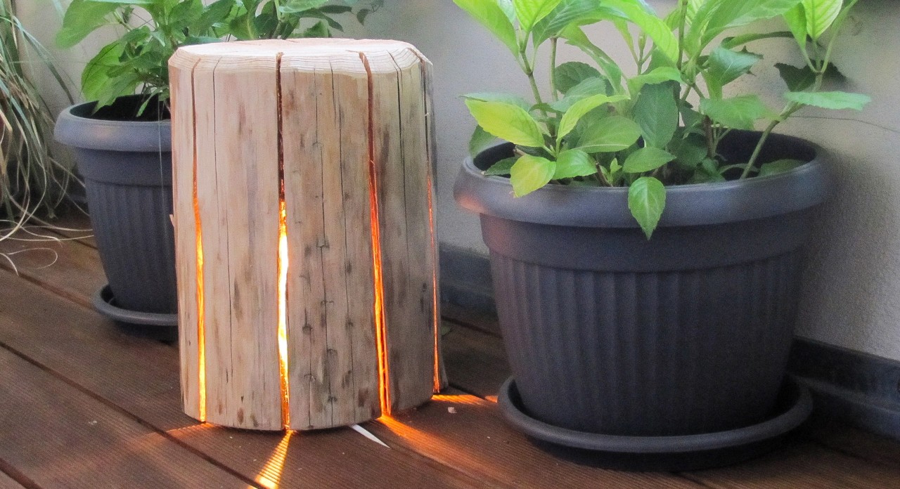 Lampa z drewna z delikatnym światłem obok donica z roślinami
