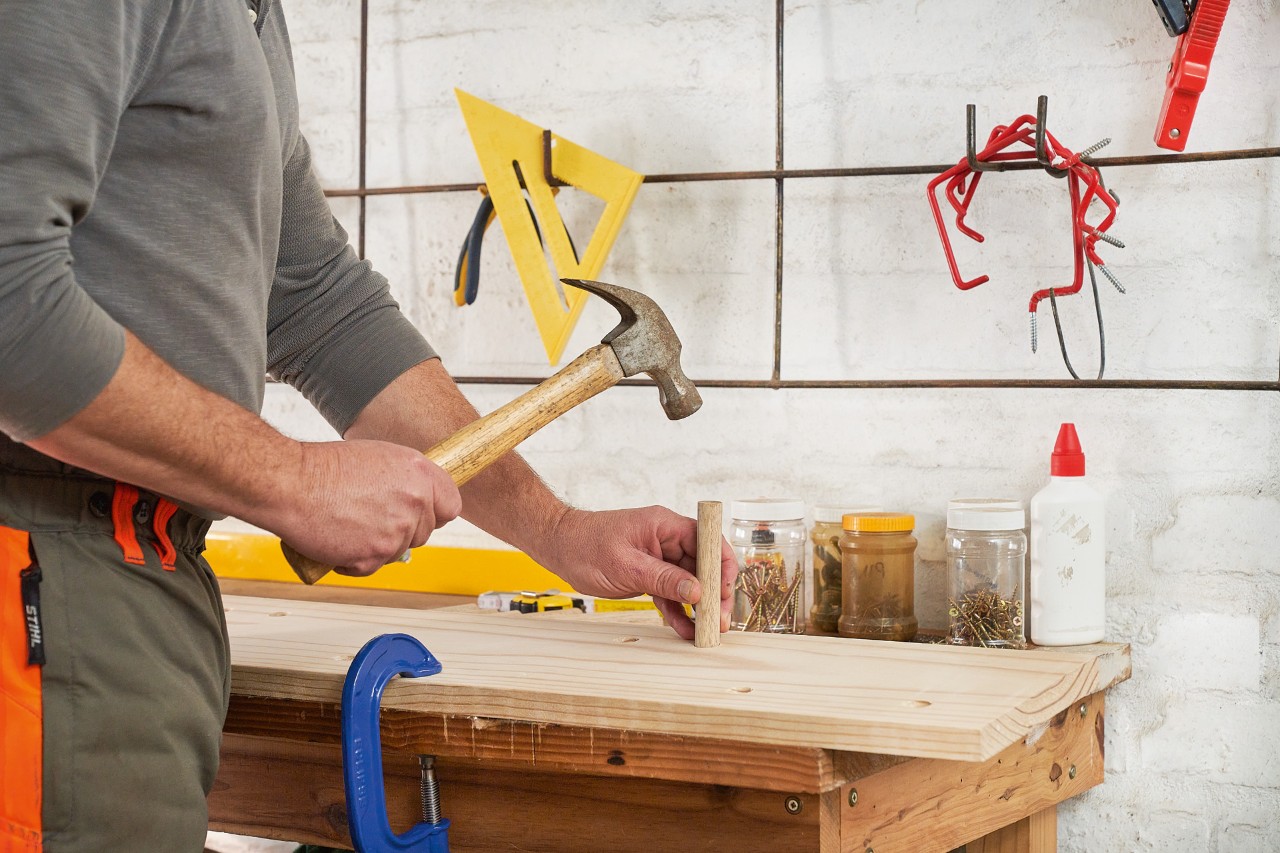 Mężczyzna wbija młotkiem pręt w otwór drewnianej deski