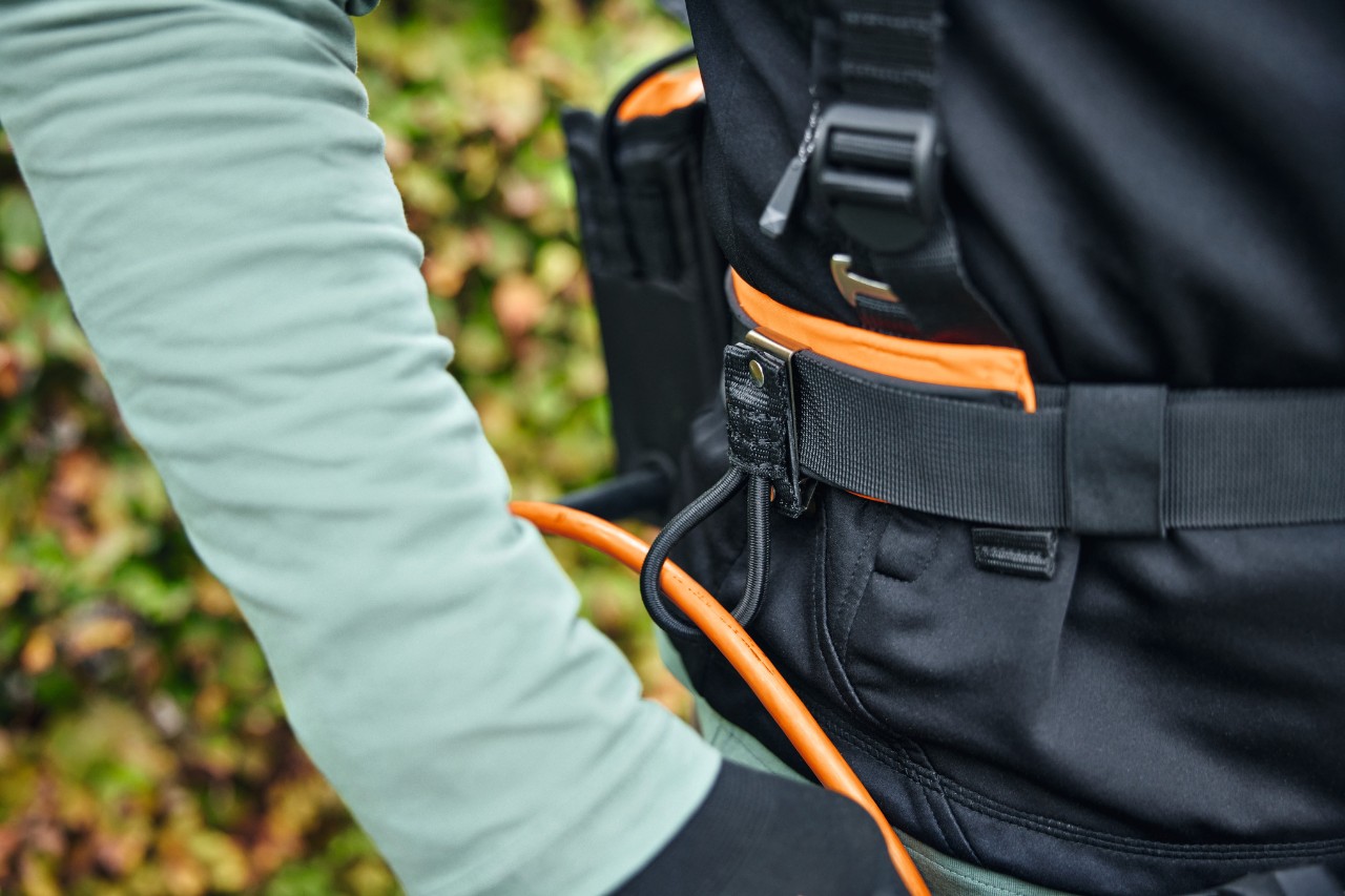 Osoba nosząca modułowy system pasów STIHL ADVANCE X-Flex, z torbą na akumulator z przewodem zasilającym i prowadnicą przewodu