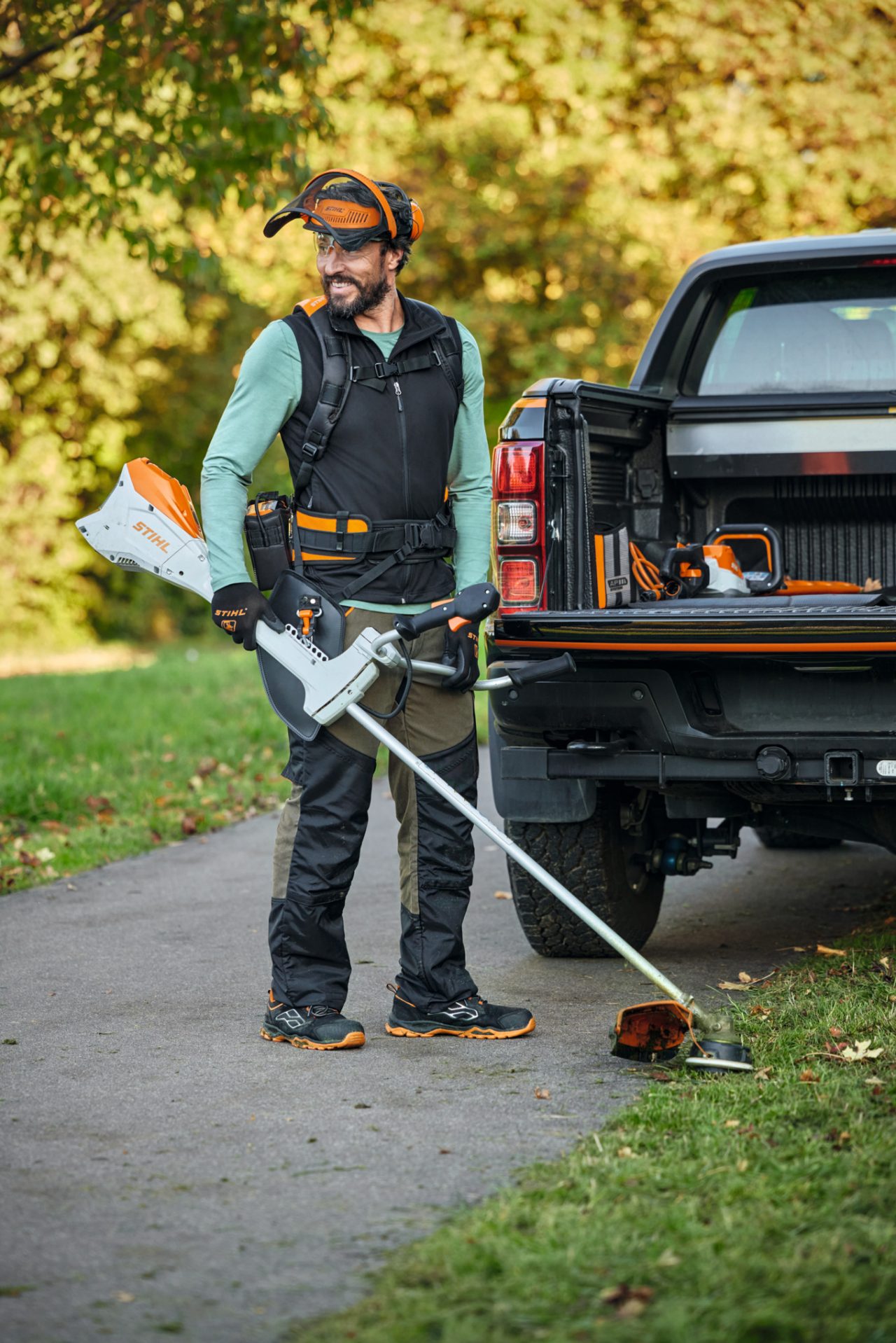 Mężczyzna z zestawem do kos mechanicznych i akumulatorową kosą mechaniczną STIHL FSA 200 stoi przed samochodem