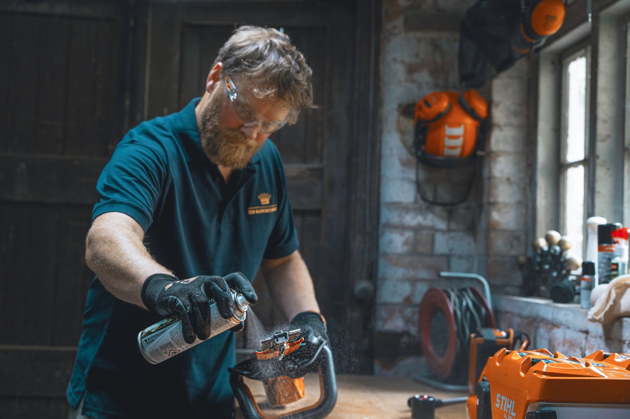Mężczyzna w warsztacie spryskuje nożyce do żywopłotu środkiem STIHL Superclean