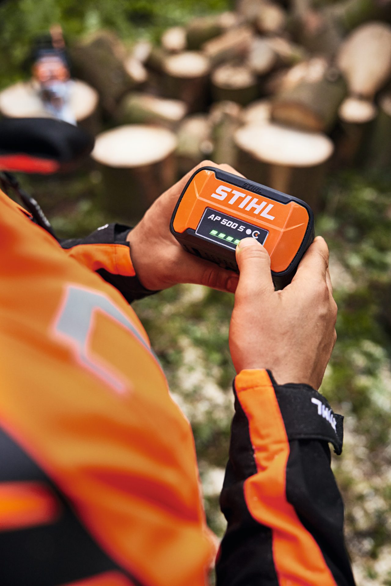Osoba trzymająca w rękach akumulator STIHL AP 500 S. Diody LED wskaźnika naładowania świecą się na zielono. 