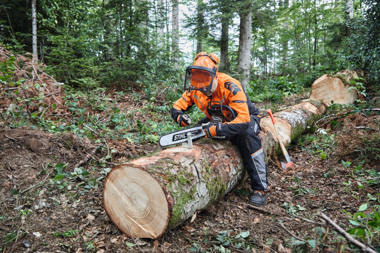 Mężczyzna w sprzęcie ochronnym tnie powalone drzewo pilarką łańcuchową STIHL z prowadnicą pełną