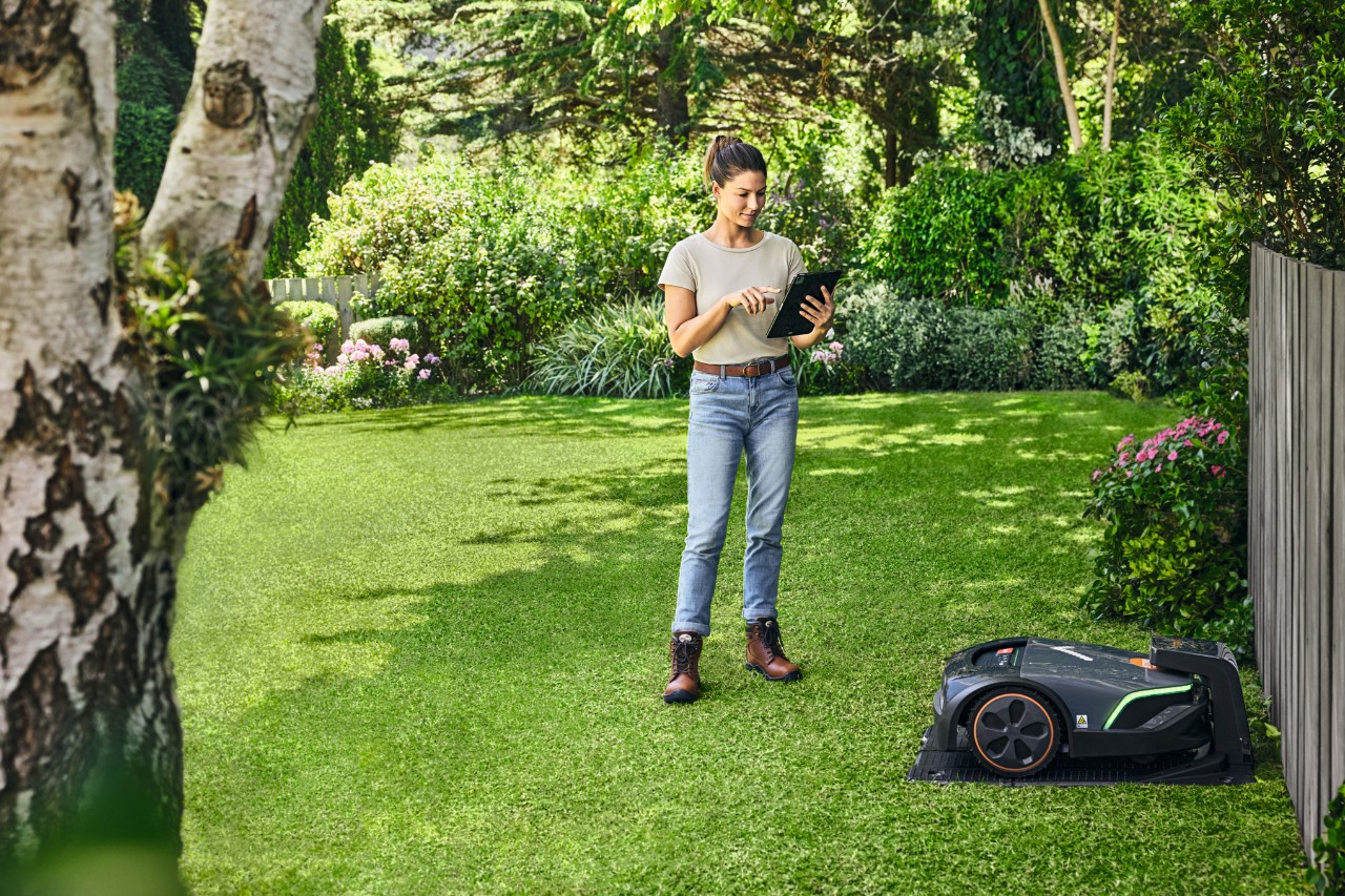 Kobieta obsługująca STIHL iMOW® EVO za pomocą tabletu w swoim ogrodzie